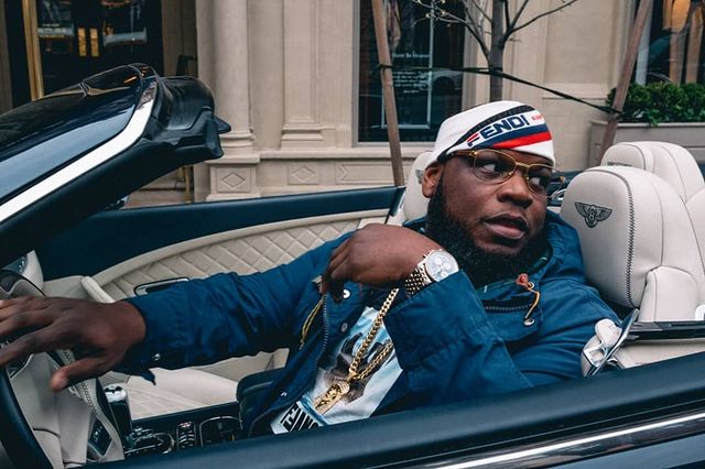 Meyhem Lauren in a blue hoodie and white cap posing in his car.